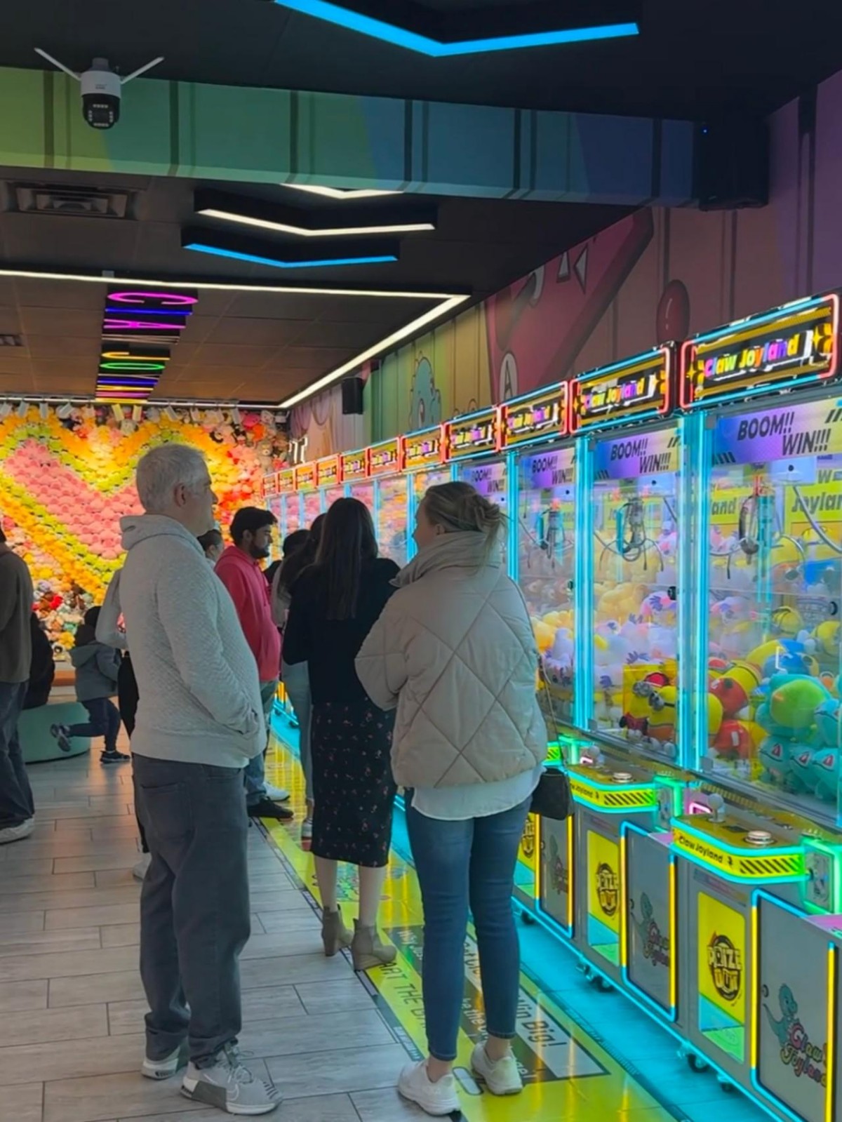 Crowded arcade prize machine area with players lining up for 4-player clip prize machines